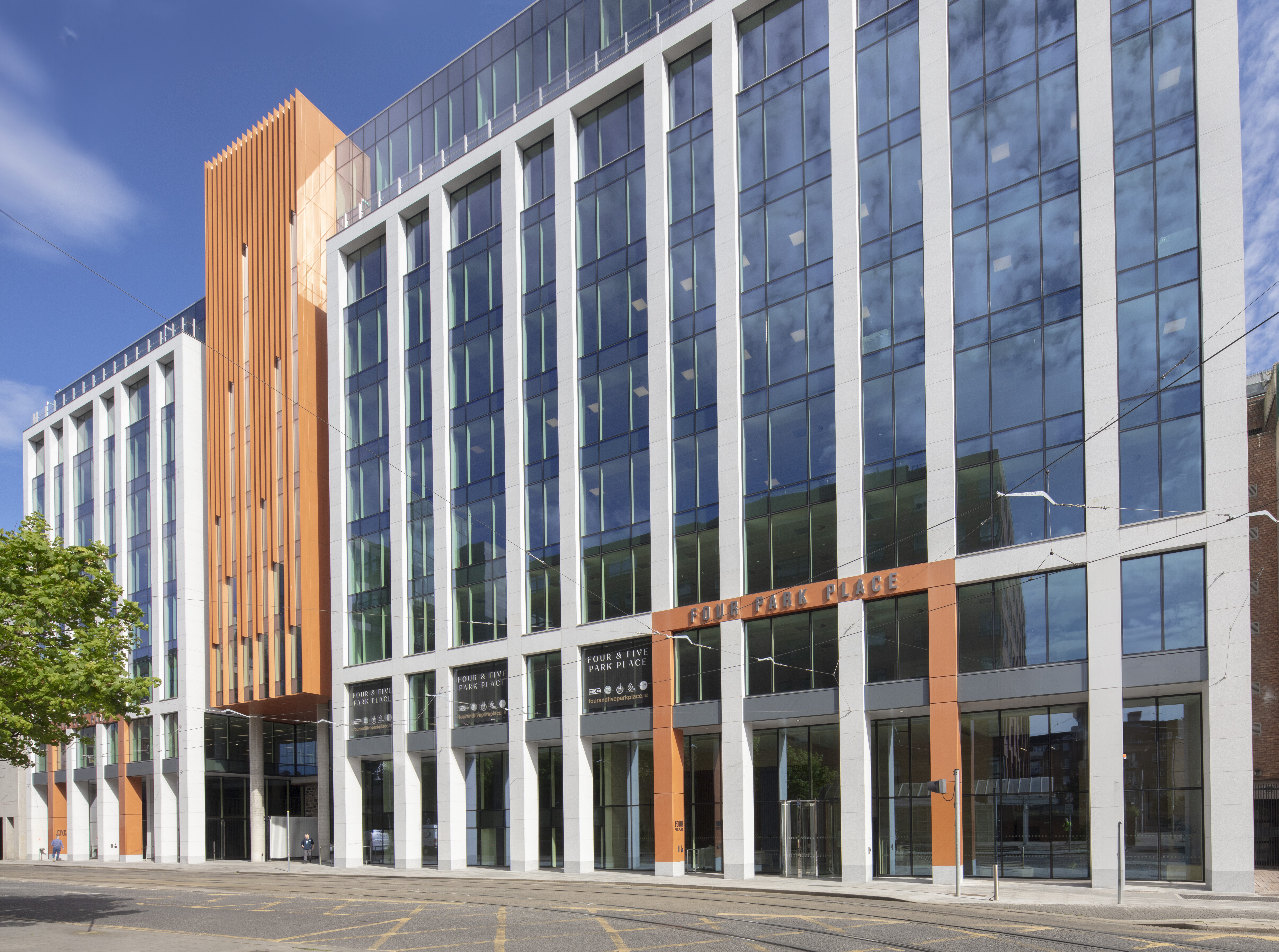 Modern building with glass and wooden panels on the facade, tall vertical elements, and an asymmetrical design, set against a clear blue sky.