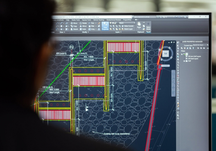 Person using a computer to view a CAD program with a technical drawing showing measurements like '3000 mm' and detailed layout lines.