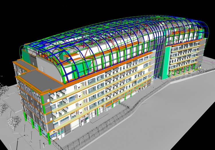 3D computer-generated model of a multi-story building with a curved, transparent roof featuring a colorful grid pattern in green and blue. The facade has layers in various colors, with orange for the outer frame and yellow for balconies or walkways. Surrounding trees and smaller structures in lighter grey indicate landscaping or adjacent buildings.