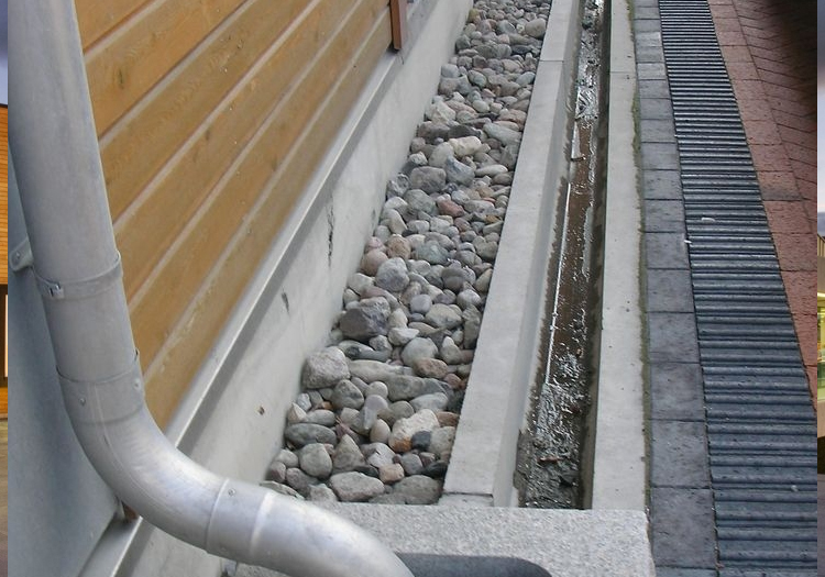 Section of building drainage infrastructure featuring a downspout connected to a gutter system. The downspout directs rainwater into a bed of rounded stones, serving as a drainage area to manage water flow and prevent soil erosion.