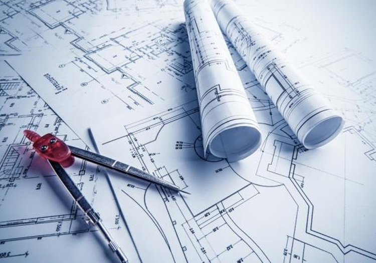 Set of architectural blueprints with detailed technical drawings of a structure. On top are two rolled-up documents, a red drawing compass, and a mechanical pencil, indicating an architect's or engineer's workspace. These tools suggest the planning phase of construction or design work.