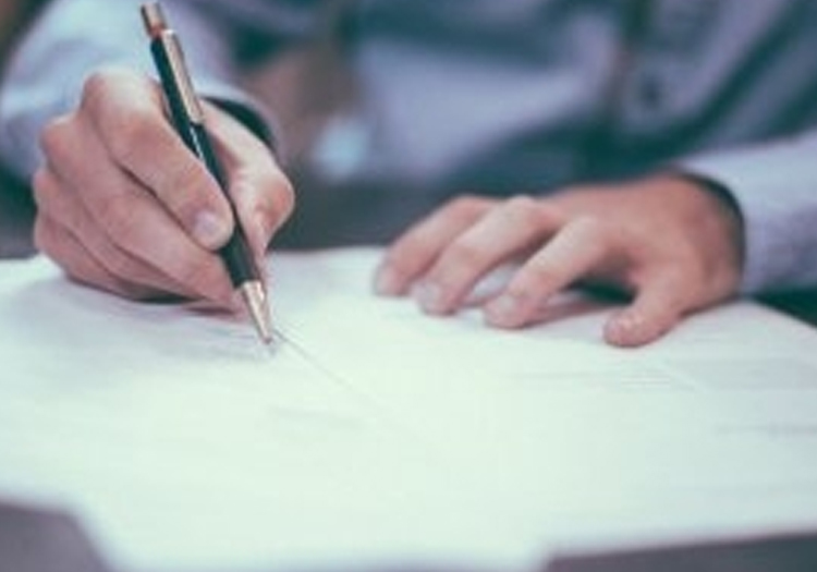 Close-up of a person’s hands writing on a sheet of paper with a pen. The focus is on the writing hand, with a blurred background emphasizing the action. Relevant for topics related to education, literacy, business, or written documentation.