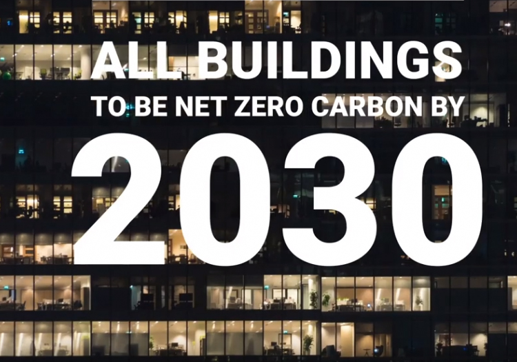 Night-time view of a building section with illuminated windows, overlaid with text 'ALL BUILDINGS TO BE NET ZERO CARBON BY 2030,' emphasizing a goal for reducing carbon footprints in architecture by the next decade