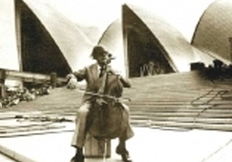 Black-and-white photograph of an individual playing the cello in front of the Sydney Opera House, giving the scene a timeless quality.