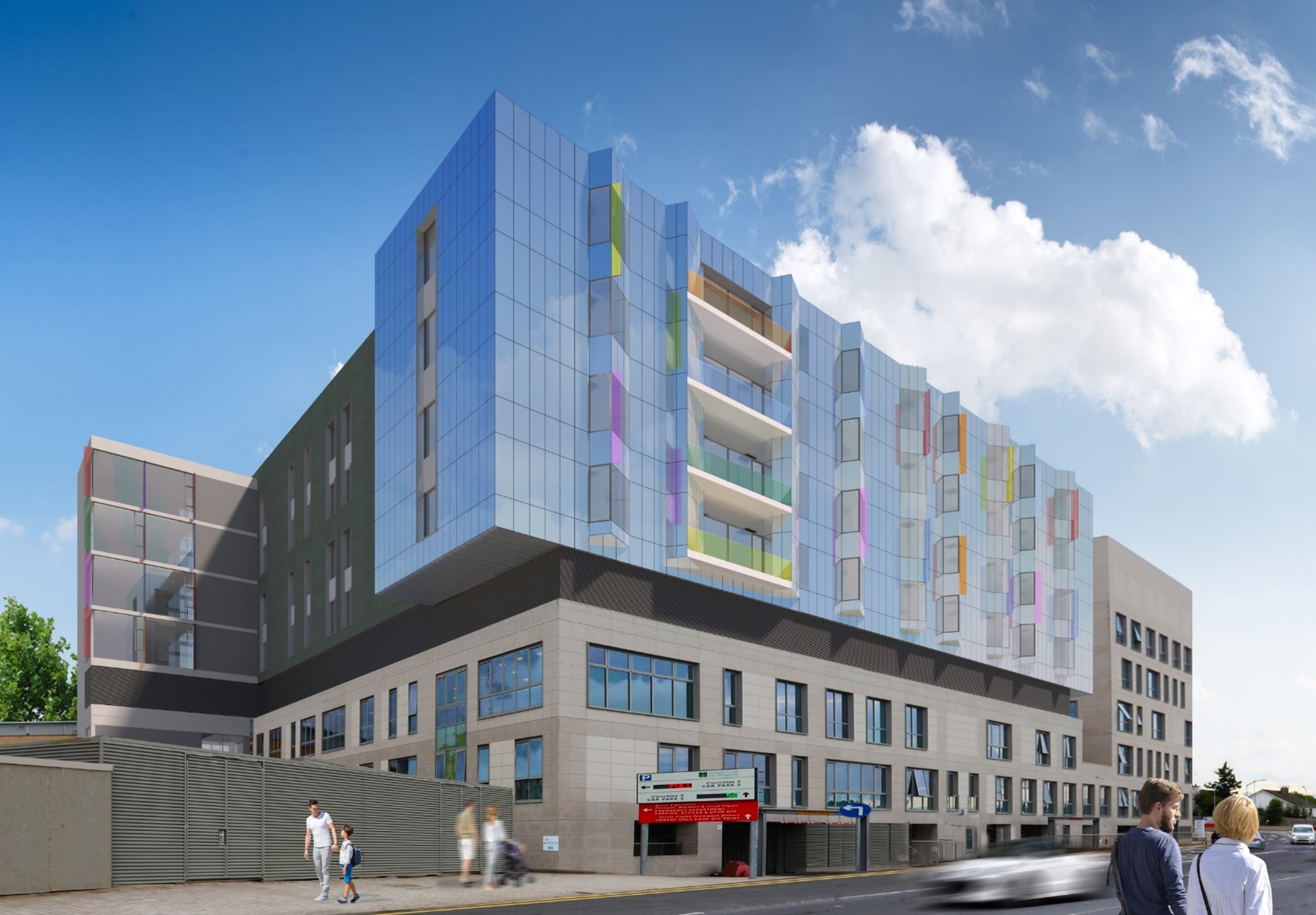 A modern multi-story building with gray and blue panels, vibrant upper-floor colors, and commercial spaces at ground level. Two people walk by, and a blurred car passes on the street under a partly cloudy sky