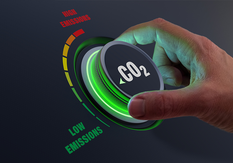 A hand turning a CO2 dial towards the "Low Emissions" section, illuminated in green, representing carbon reduction efforts.